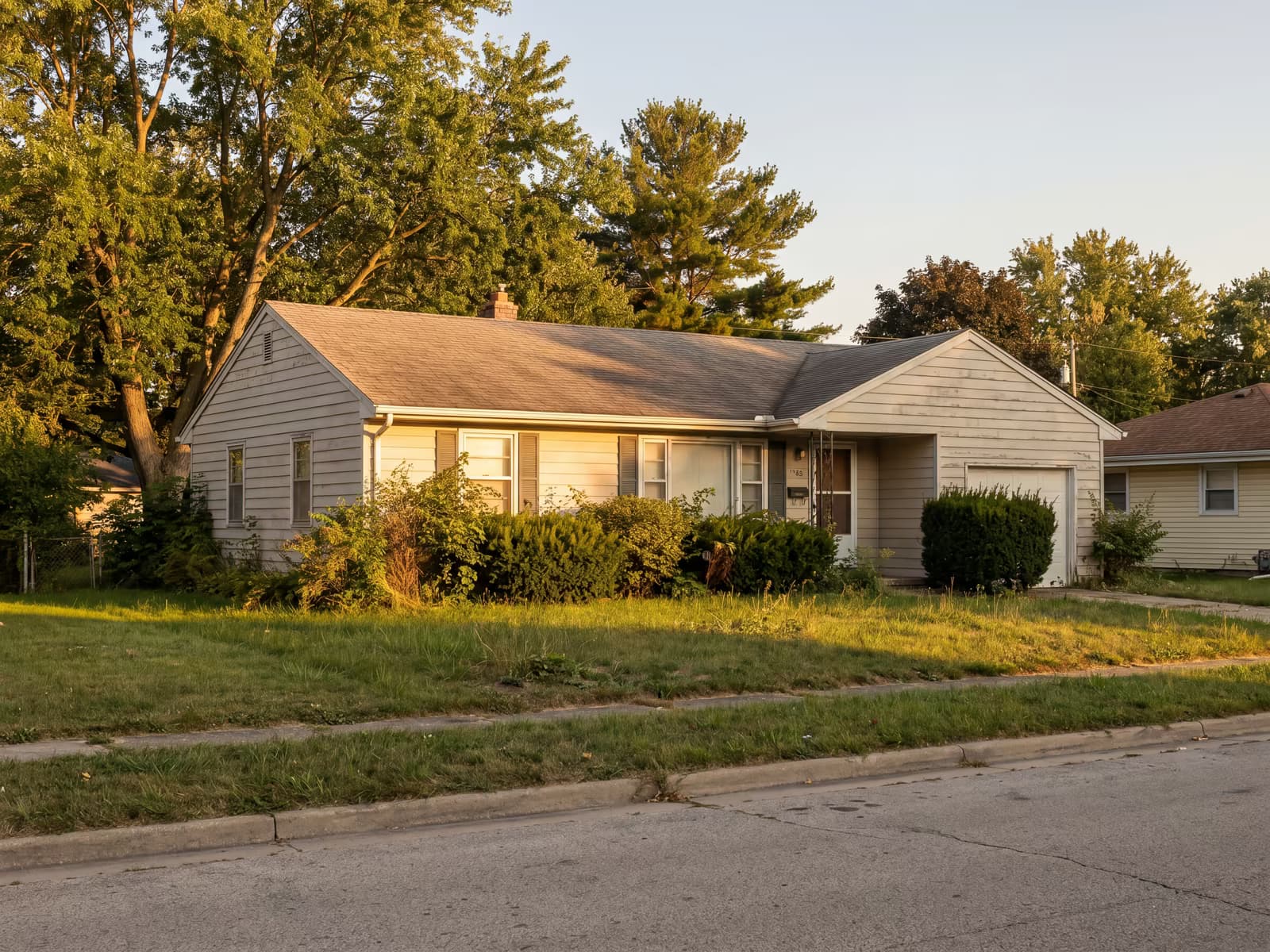 Modest single-family home exterior at golden hour with a slightly overgrown lawn